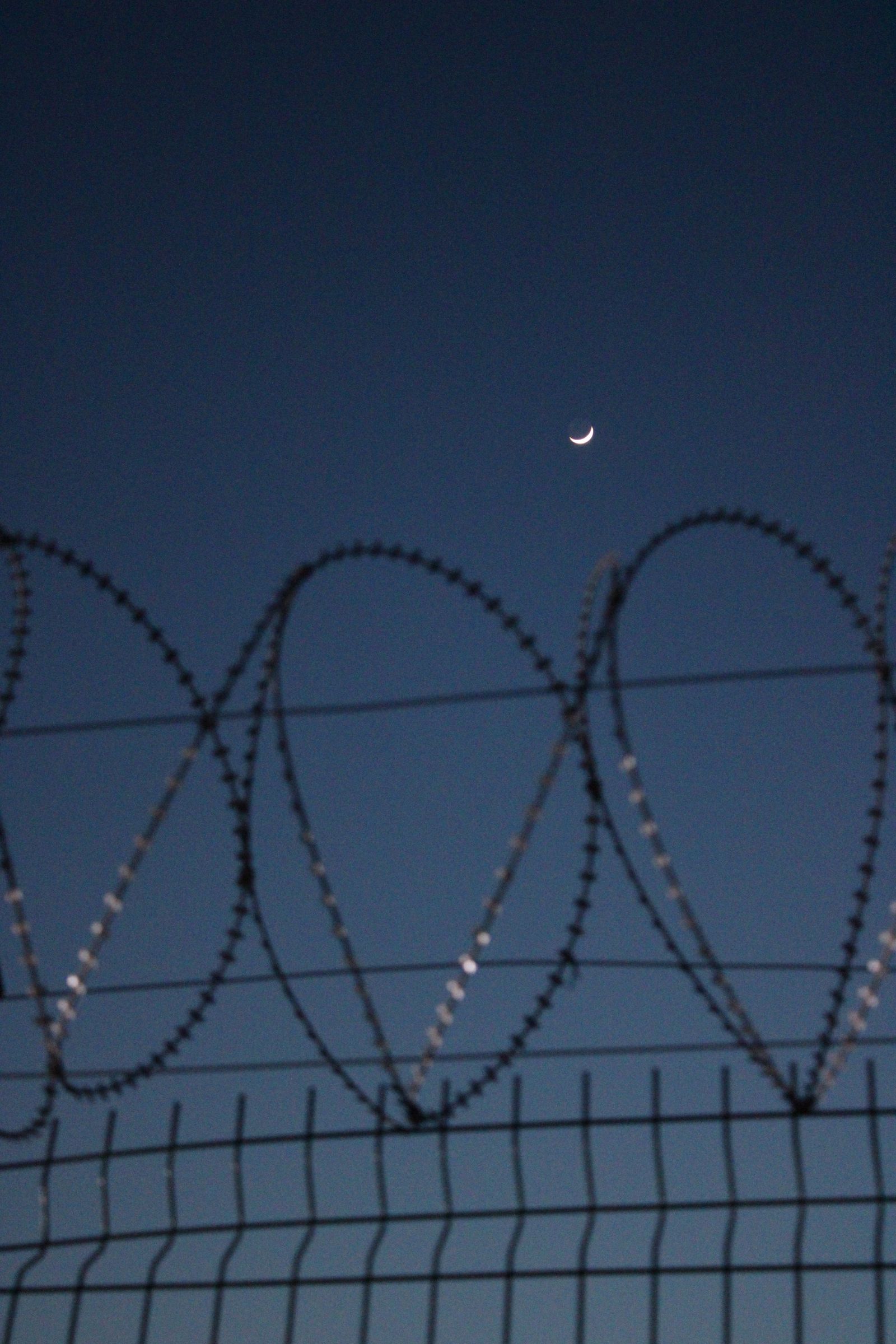Barbed wire silhouette at night — the core scene of border and critical infrastructure security